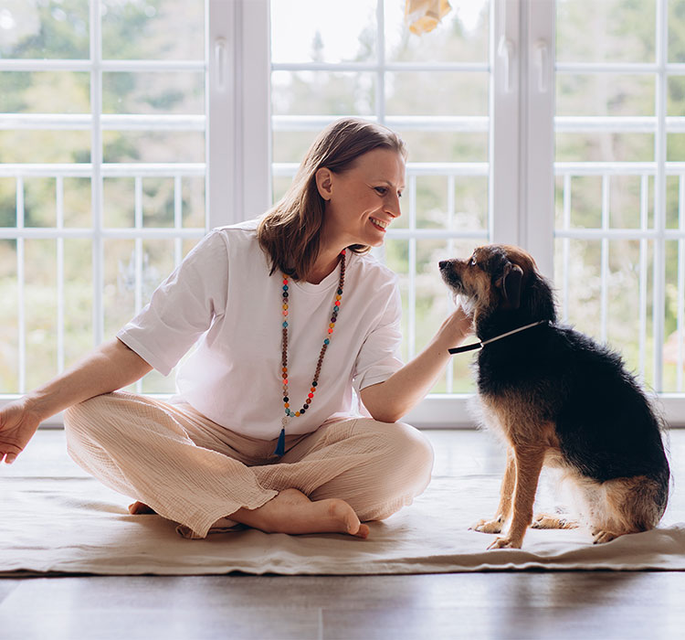 Middle aged woman practices Kundalini yoga at home with her dog nearby. Spiritual balance, feminine energy, harmony, mindfulness, and emotional wellness with animals